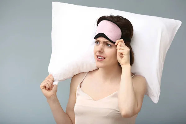 Gestresste Frau mit Schlafmaske und Kopfkissen auf farbigem Hintergrund — Stockfoto