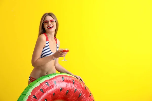 Schöne junge Frau mit aufblasbarem Ring und Cocktail auf farbigem Hintergrund — Stockfoto