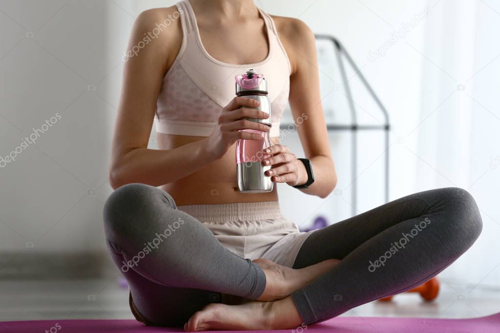 Sporty young woman drinking water indoors
