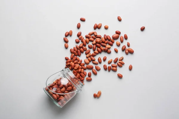 Overturned jar with tasty peanuts on light background — Stock Photo, Image