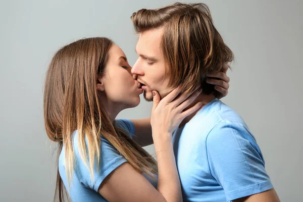 Küsst junges Paar auf grauem Hintergrund — Stockfoto
