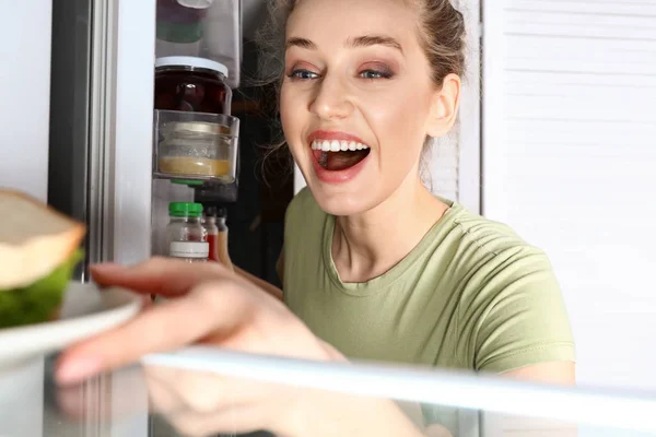 Joyeux jeune femme choisissant la nourriture au réfrigérateur, vue de l'intérieur — Photo
