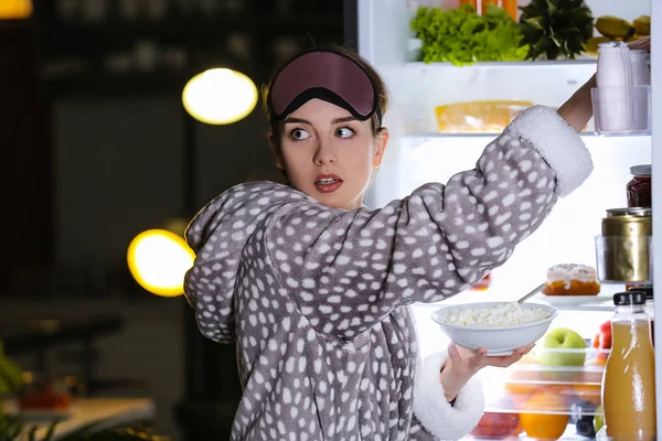 Mujer joven cautelosa eligiendo comida en el refrigerador por la noche —  Fotos de Stock