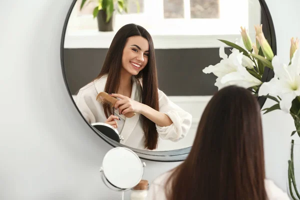 Gyönyörű fiatal nő hullámzó ő egészséges, hosszú haj közelében tükör otthon — Stock Fotó
