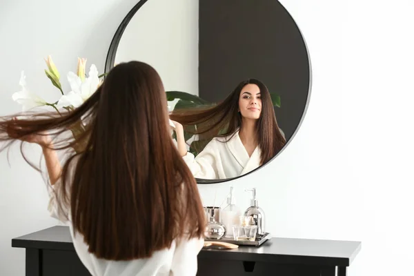 Mulher bonita com cabelo longo saudável olhando no espelho em casa — Fotografia de Stock