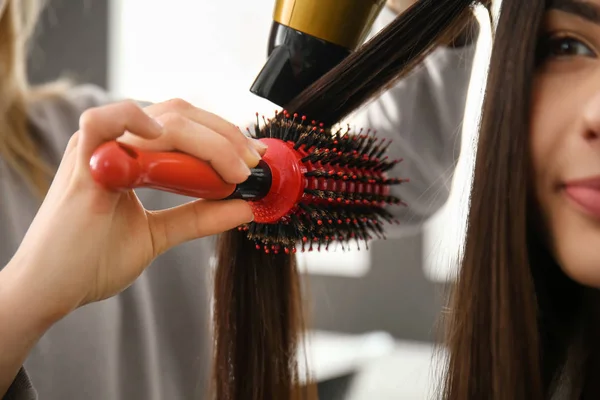 Cabeleireiro com secador de cabelo escovação cabelo longo de mulher jovem no salão — Fotografia de Stock