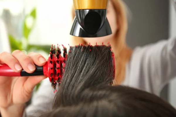 Coiffeur avec sèche-cheveux brossant les cheveux longs de la jeune femme dans le salon — Photo