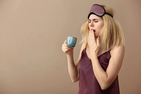 Donna assonnata con maschera e tazza di caffè su sfondo di colore — Foto Stock