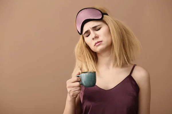 Slaperige vrouw met masker en kop koffie op kleur achtergrond — Stockfoto