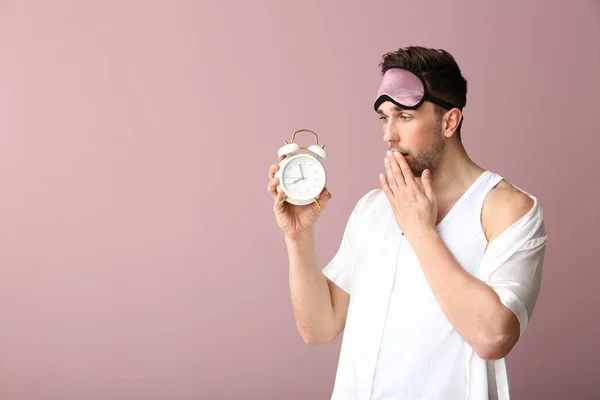 Jovem com máscara de sono e despertador no fundo de cor — Fotografia de Stock