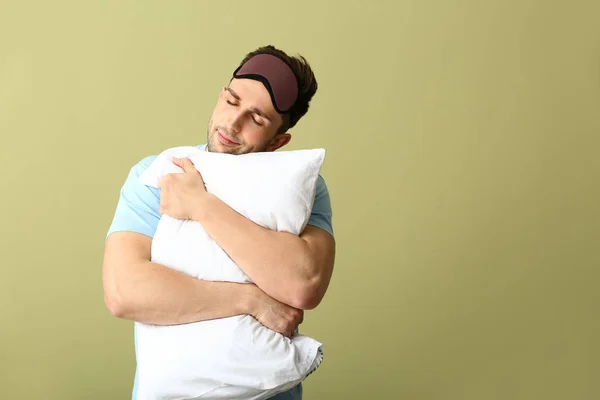 Hombre joven con máscara de sueño y almohada sobre fondo de color — Foto de Stock