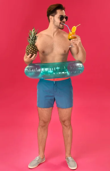 Przystojny człowiek z nadmuchiwanym pierścieniem, ananasem i koktajlem na kolorowym tle — Zdjęcie stockowe