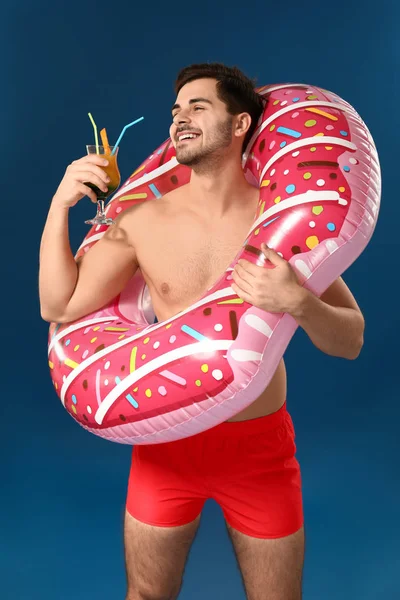 Handsome man with inflatable ring and cocktail on color background — Stock Photo, Image