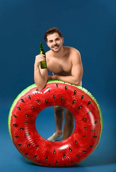 Красивый мужчина с надувным кольцом и пивом на цветном фоне — стоковое фото
