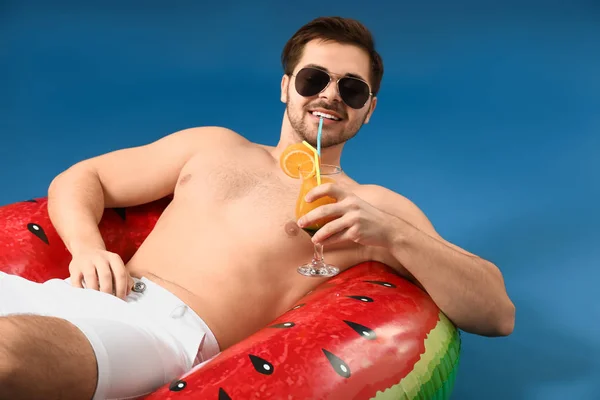 Handsome man with cocktail relaxing on inflatable ring against color background — Stock Photo, Image