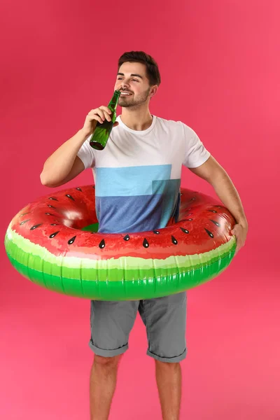 Homem bonito com anel inflável e cerveja no fundo da cor — Fotografia de Stock