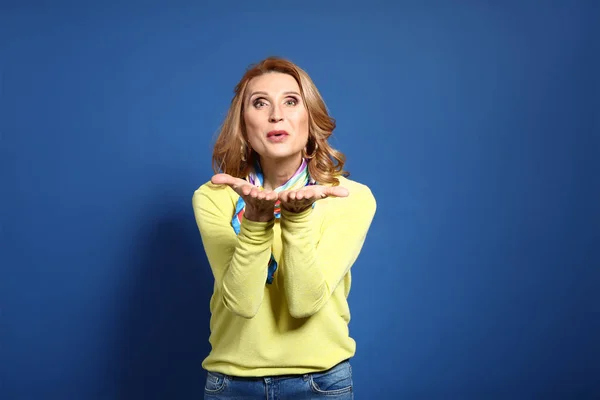 Fashionable mature woman blowing kiss on color background — Stock Photo, Image