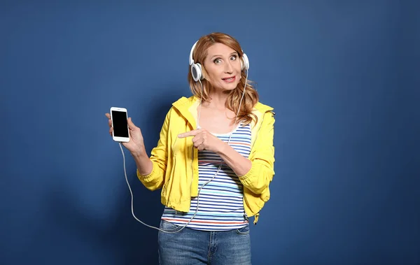 Dospělá žena naslouchající hudbě na barevném pozadí — Stock fotografie