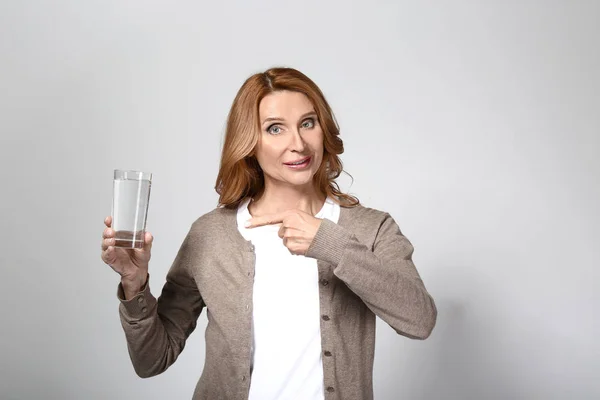 Rijpe vrouw met glas water op grijze achtergrond — Stockfoto