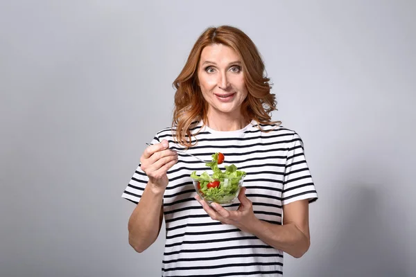 Mature woman with bowl of vegetable salad on grey background — Stock Photo, Image