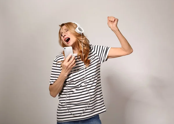 Reife Frau hört Musik und singt auf grauem Hintergrund — Stockfoto