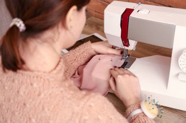 Female tailor working on sewing machine in atelier clipart