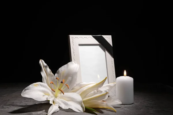 Blank funeral frame, burning candle and flowers on table against dark background