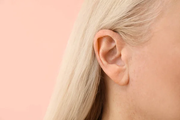 Mature woman with hearing problem on color background, closeup