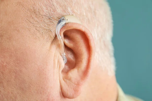 Senior man with hearing aid on grey background, closeup — Stock Photo, Image