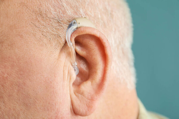 Старший мужчина со слуховым аппаратом на сером фоне, крупным планом
