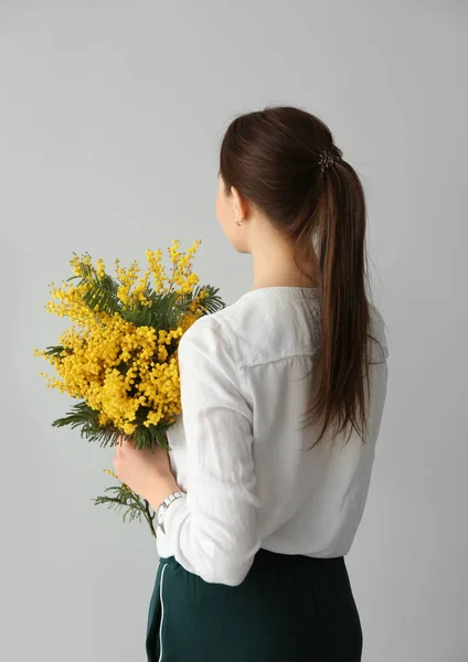 Young woman holding bouquet of beautiful mimosa flowers on light background — Stock Photo, Image