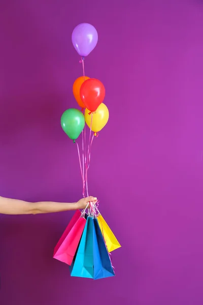 Weibliche Hand mit Geschenken und Luftballons auf farbigem Hintergrund — Stockfoto