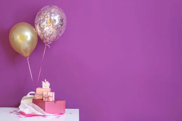 Schöne Geschenke mit Luftballons auf dem Tisch vor farbigem Hintergrund — Stockfoto