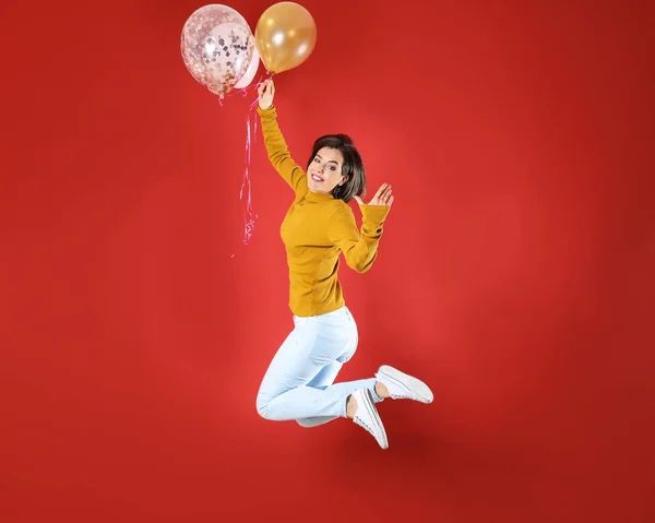 Springen jonge vrouw met lucht ballonnen tegen kleur achtergrond — Stockfoto