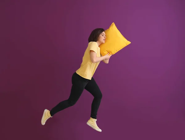 Jumping young woman with pillow against color background — Stock Photo, Image