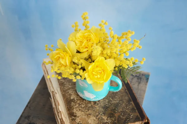 Cup with beautiful yellow flowers and old book on color background — Stock Photo, Image