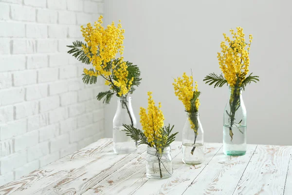 Cristalería con hermosas flores mimosa sobre mesa blanca en la habitación — Foto de Stock