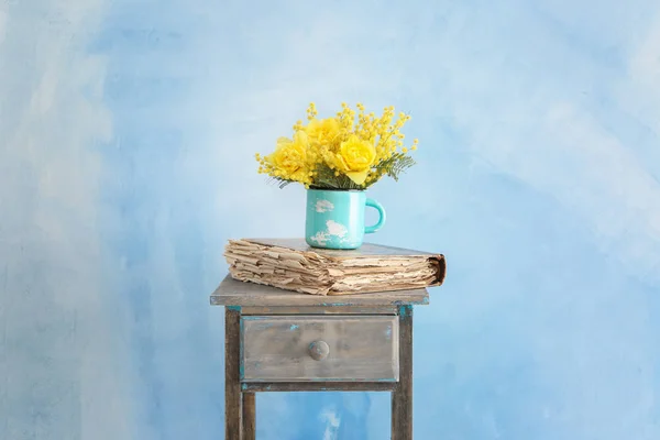 Coupe avec de belles fleurs jaunes et vieux livre sur la table sur fond de couleur — Photo