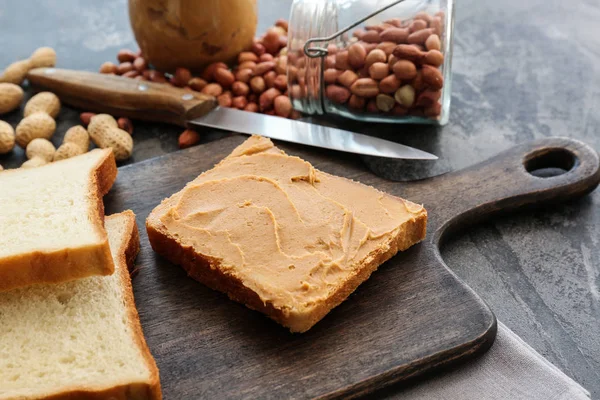 Placa de madeira com manteiga de amendoim saborosa e pão na mesa — Fotografia de Stock