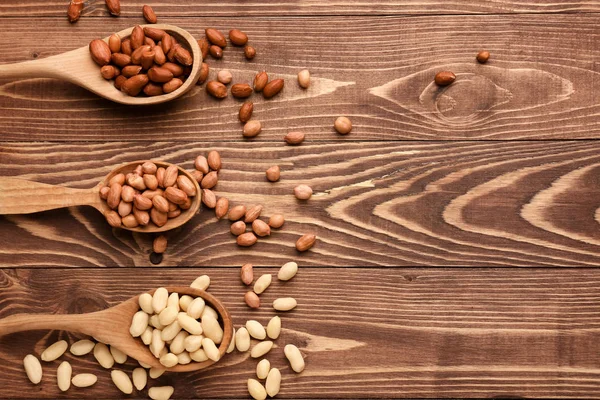 Colheres com amendoins saborosos no fundo de madeira — Fotografia de Stock