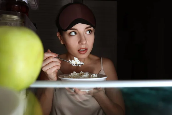 Mujer joven y cautelosa comiendo comida cerca de la nevera, vista desde el interior —  Fotos de Stock