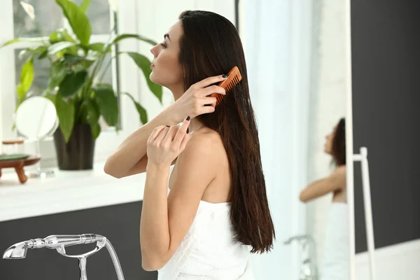 Mulher bonita aplicando cosméticos em seu cabelo longo saudável em casa — Fotografia de Stock