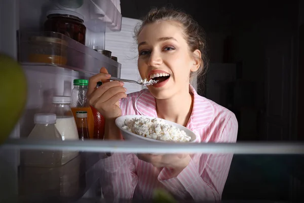 Krásná mladá žena jedla jídlo blízko ledničky, pohled zevnitř — Stock fotografie