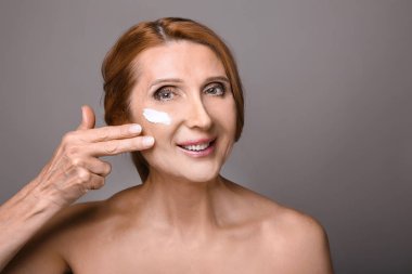 Olgun kadın yüz kremi gri arka plan üzerinde uygulama