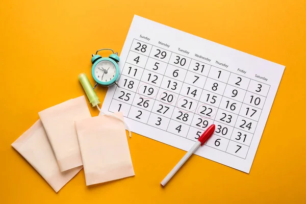 Menstrual calendar with feminine products and alarm clock on color background — Stock Photo, Image