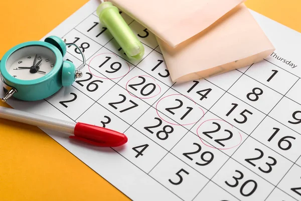Calendario menstrual con productos femeninos y despertador sobre fondo de color — Foto de Stock
