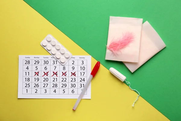 Менструальный календарь с женскими продуктами и таблетками на цветном фоне — стоковое фото