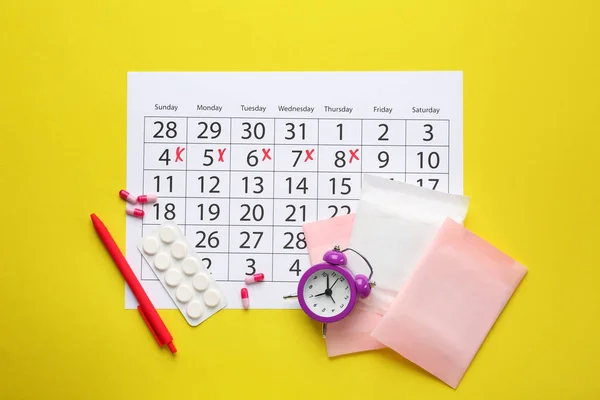 Menstrual calendar with pads, pills and alarm clock on color background — Stock Photo, Image