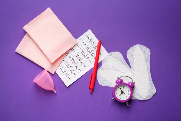 Menstrual calendar with feminine products and alarm clock on color background — Stock Photo, Image