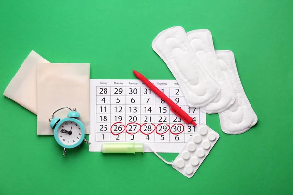 Menstruatiekalender met vrouwelijke producten, pillen en wekker op kleur achtergrond — Stockfoto